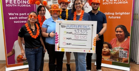 future metals Six people celebrate near Future Metals’ aerospace-grade titanium alloy display at Feeding South Florida, banners highlighting supply chain compliance.