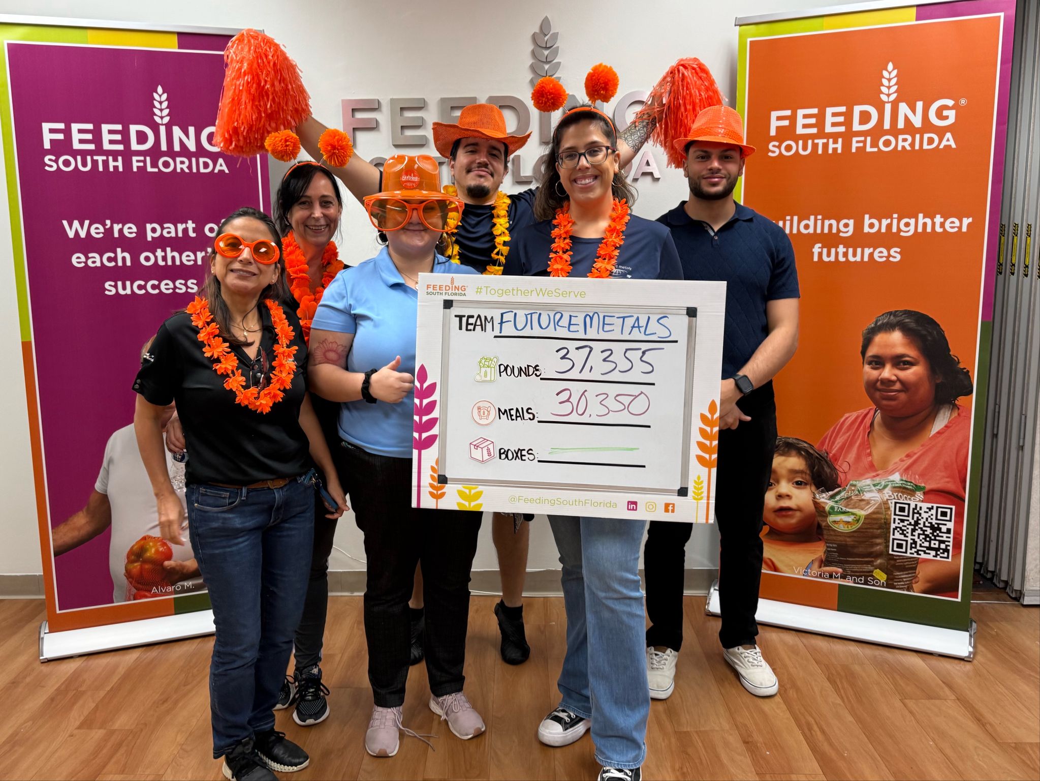 future metals Six people celebrate near Future Metals’ aerospace-grade titanium alloy display at Feeding South Florida, banners highlighting supply chain compliance.